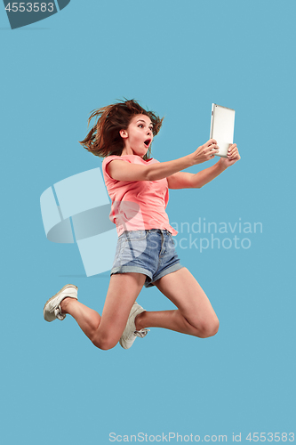 Image of Image of young woman over blue background using laptop computer or tablet gadget while jumping.