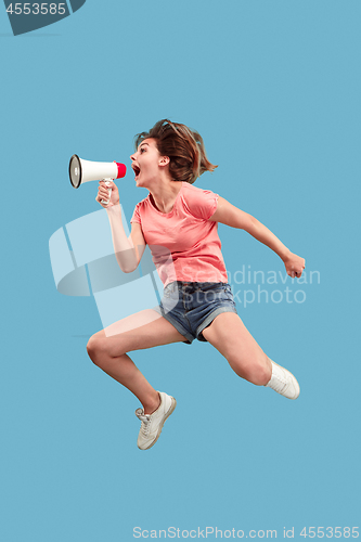 Image of Beautiful young woman jumping with megaphone isolated over blue background