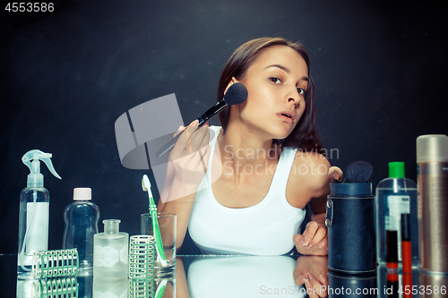 Image of Beauty woman applying makeup. Beautiful girl looking in the mirror and applying cosmetic with a big brush.