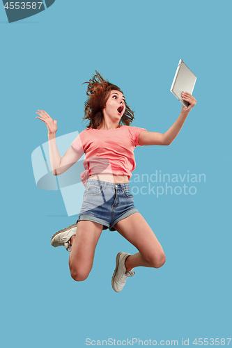 Image of Image of young woman over blue background using laptop computer or tablet gadget while jumping.