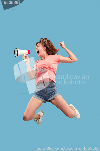 Image of Beautiful young woman jumping with megaphone isolated over blue background