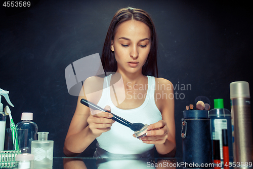 Image of Beauty woman applying makeup. Beautiful girl looking in the mirror and applying cosmetic with a big brush.