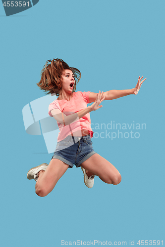 Image of Freedom in moving. Pretty young woman jumping against blue background