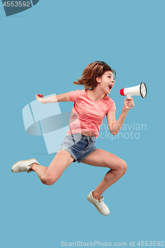 Image of Beautiful young woman jumping with megaphone isolated over blue background