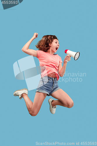 Image of Beautiful young woman jumping with megaphone isolated over blue background