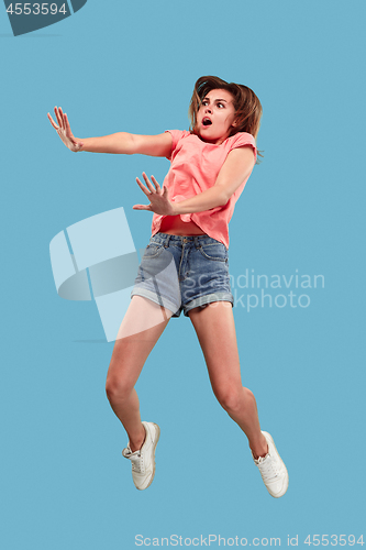 Image of Freedom in moving. Pretty young woman jumping against blue background