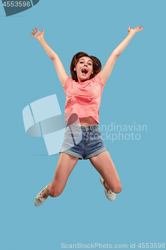 Image of Freedom in moving. Pretty young woman jumping against blue background