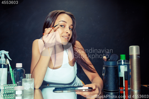 Image of Beauty woman applying makeup. Beautiful girl looking in the mirror and applying cosmetic with a brush.