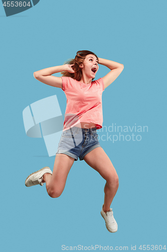 Image of Freedom in moving. Pretty young woman jumping against blue background