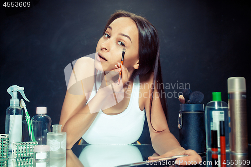 Image of Beauty woman applying makeup. Beautiful girl looking in the mirror and applying cosmetic with a brush.