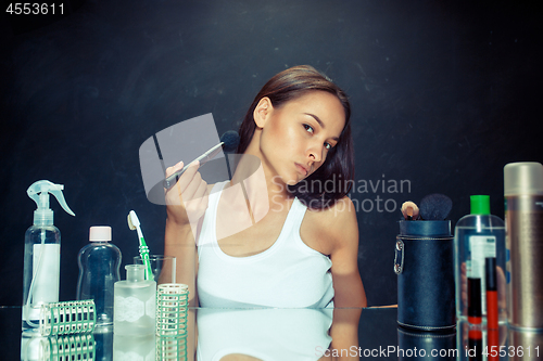 Image of Beauty woman applying makeup. Beautiful girl looking in the mirror and applying cosmetic with a big brush.