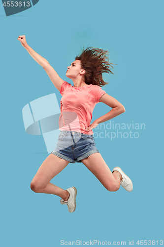 Image of Freedom in moving. Pretty young woman jumping against blue background