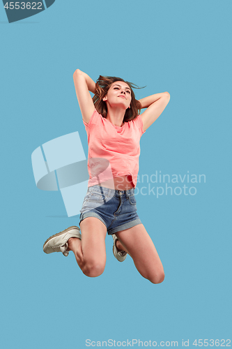 Image of Freedom in moving. Pretty young woman jumping against blue background