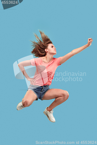 Image of Freedom in moving. Pretty young woman jumping against blue background