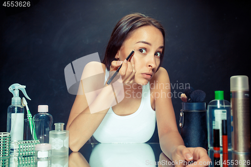 Image of Beauty woman applying makeup. Beautiful girl looking in the mirror and applying cosmetic with a Eyeliner.