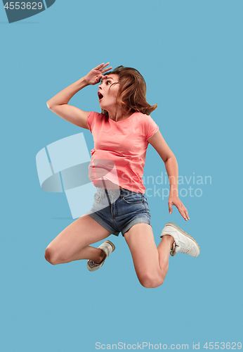 Image of Freedom in moving. Pretty young woman jumping against blue background