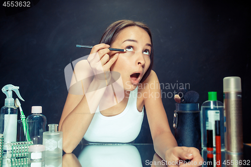 Image of Beauty woman applying makeup. Beautiful girl looking in the mirror and applying cosmetic with a Eyeliner.