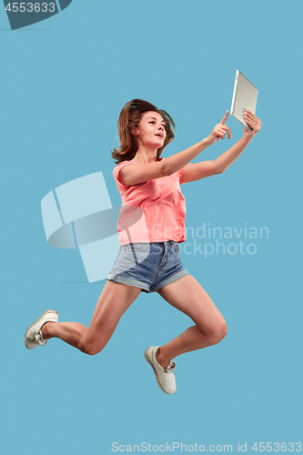 Image of Image of young woman over blue background using laptop computer or tablet gadget while jumping.