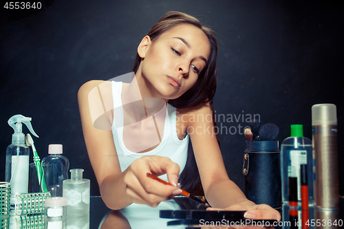 Image of Beauty woman applying makeup. Beautiful girl looking in the mirror and applying cosmetic with a brush.
