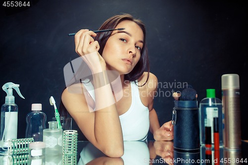 Image of Beauty woman applying makeup. Beautiful girl looking in the mirror and applying cosmetic with a brush.