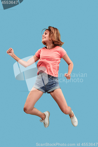 Image of Freedom in moving. Pretty young woman jumping against blue background