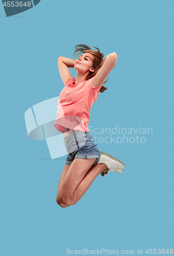 Image of Freedom in moving. Pretty young woman jumping against blue background