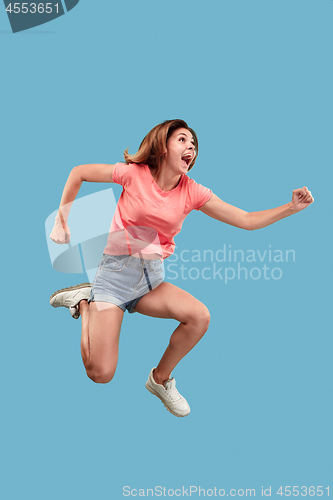 Image of Freedom in moving. Pretty young woman jumping against blue background