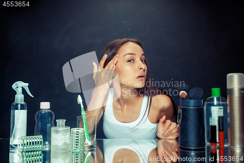 Image of Unsatisfied young woman looking at her self in mirror on black background