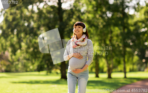 Image of happy pregnant asian woman in headphones at park