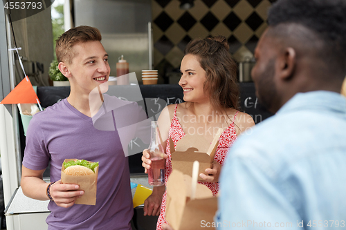 Image of happy friends with drinks eating at food truck