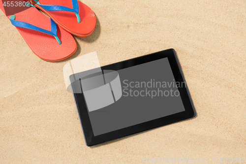 Image of tablet computer and flip flops on beach sand