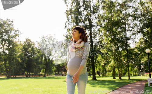 Image of happy pregnant asian woman walking at park