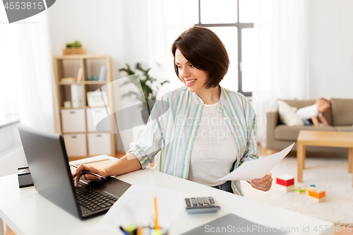 Image of mother working at laptop and baby boy at home