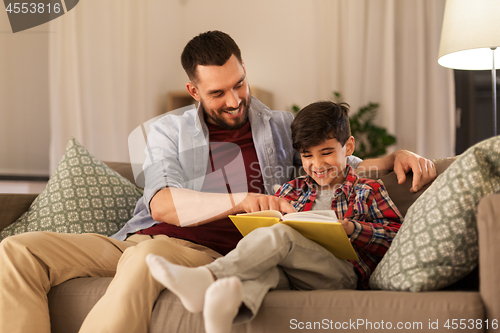 Image of happy father and son reading book sofa at home