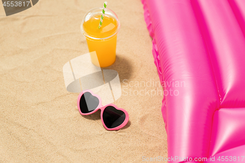 Image of sunglasses, juice and pool mattress on beach sand