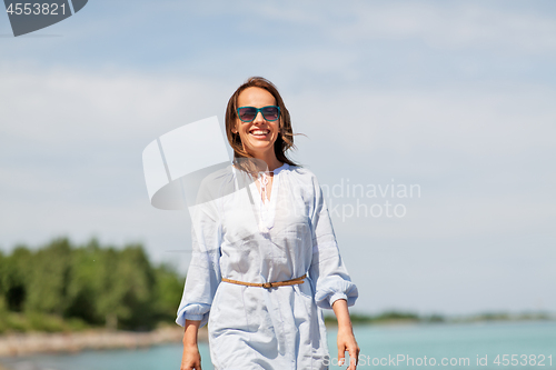 Image of happy smiling woman walking along summer beach