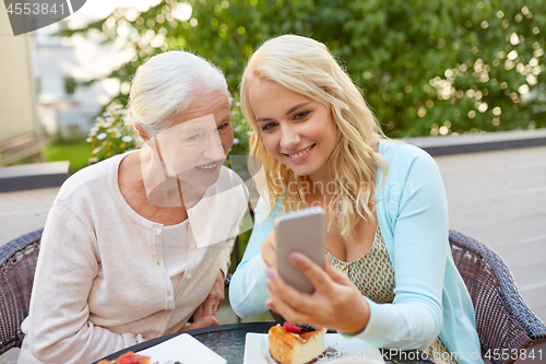 Image of daughter and senior mother with smartphone at cafe