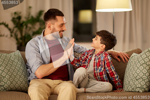 Image of father and son making high five at home in evening