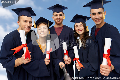 Image of happy graduates with diplomas taking selfie