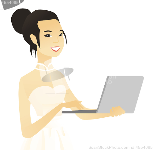 Image of Young asian bride in a white dress using a laptop.