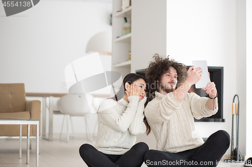 Image of multiethnic couple using tablet computer in front of fireplace