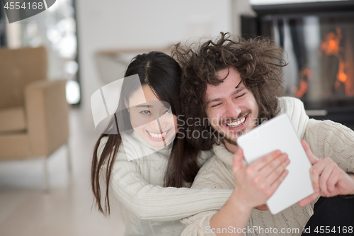 Image of multiethnic couple using tablet computer in front of fireplace