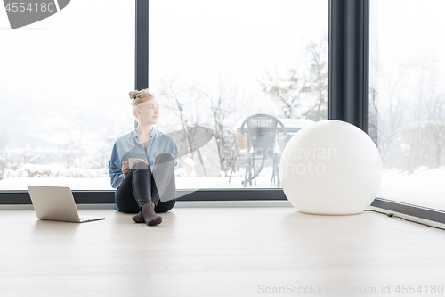 Image of woman drinking coffee and using laptop at home