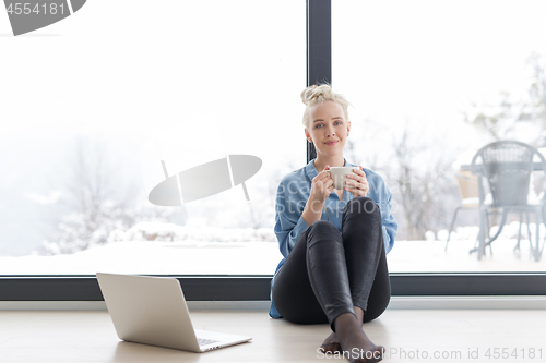 Image of woman drinking coffee and using laptop at home