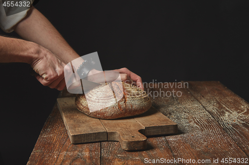 Image of on wooden board man slicing fresh organic bread