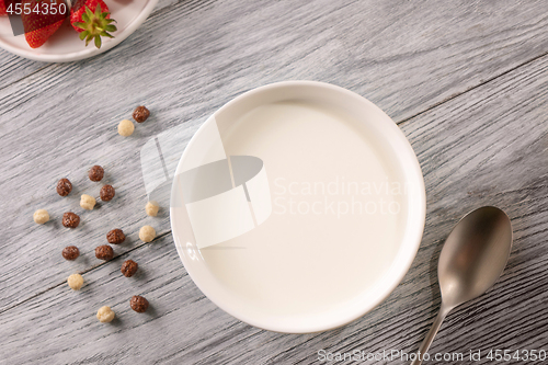 Image of Cereal balls, a plate plate of milk and a strawberry on a gray wooden table. Top view