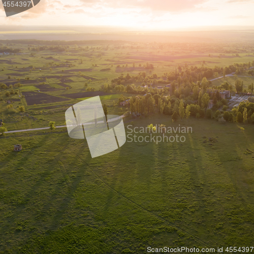 Image of Aerial view from the drone, a bird\'s eye view of abstract geometric forms of agricultural fields with a dirt road through them in the summer evening at sunset.