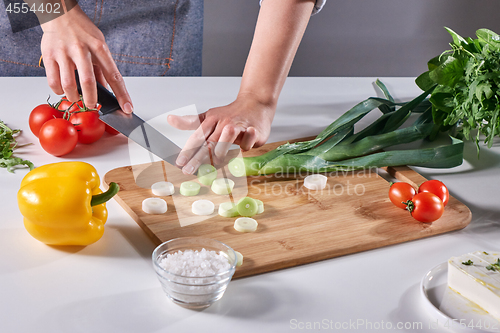 Image of Woman\'s hands cut green leek on a wooden board on the kitchen table with various fresh vegetables. Step by Step Salad Cooking