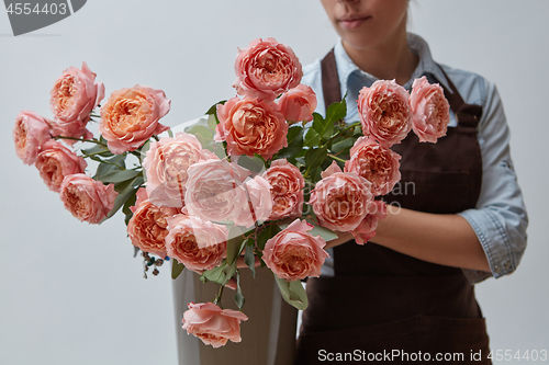 Image of A girl in a brown apron holds a vase with pink roses on a gray background. Flower concept. Gift for celebration