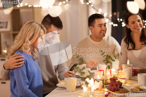 Image of happy friends with smartphone at tea party at home